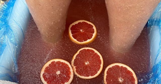 Feet soaking in a pedicure foot bath with slices of fresh grapefruit